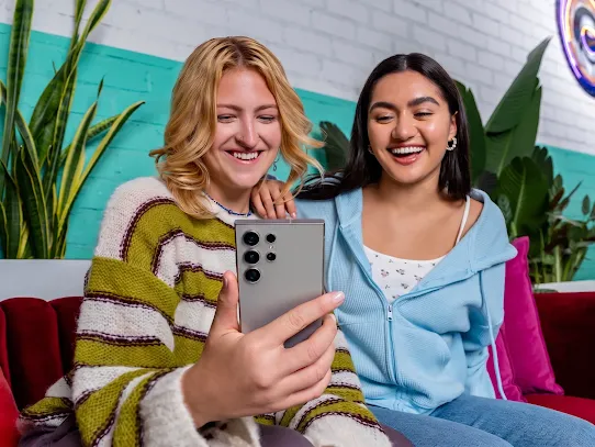 Duas jovens sorrindo enquanto usam um celular Android.