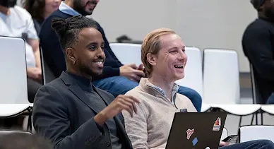 One person in the audience, with a laptop in front, is talking and smiling at the host.