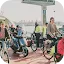 A large group of commuters on bicycles and a motor scooter waiting on a ferry crossing a river.