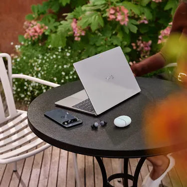 Googlebook open on an outdoor café table with a phone and earbuds.