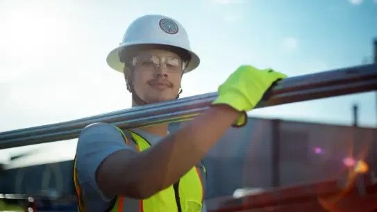 Person carrying metal polls with safety hat and gear
