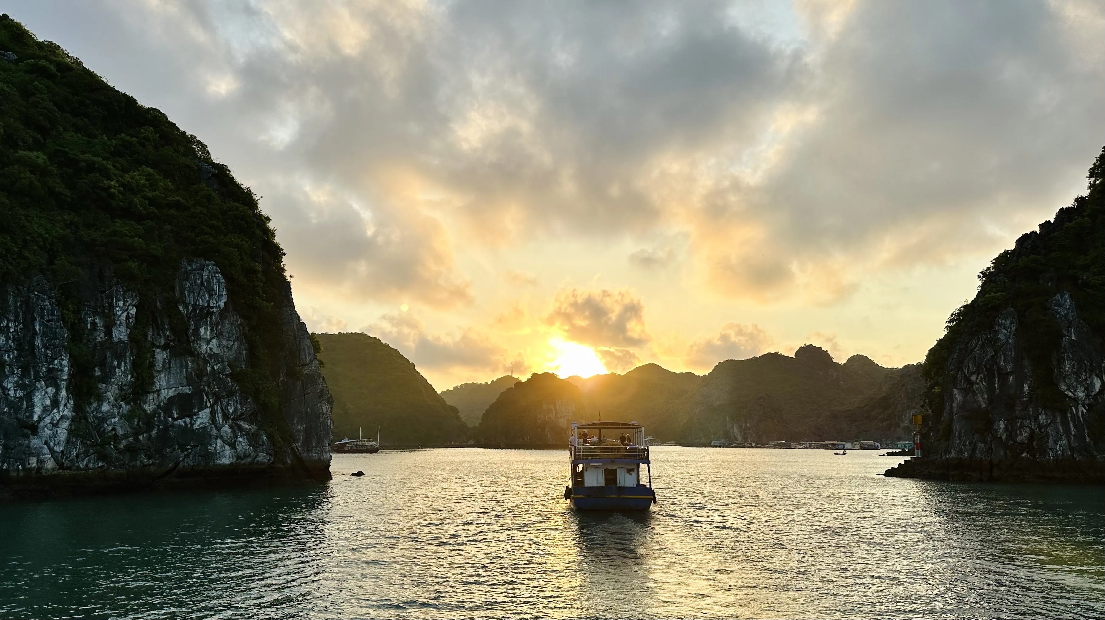 Sunset over a bay in Việt Nam with a boat and limestone islands.