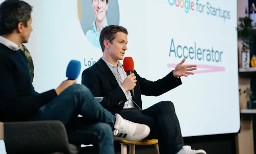 Two individuals on stage, holding microphones and speaking at the event.