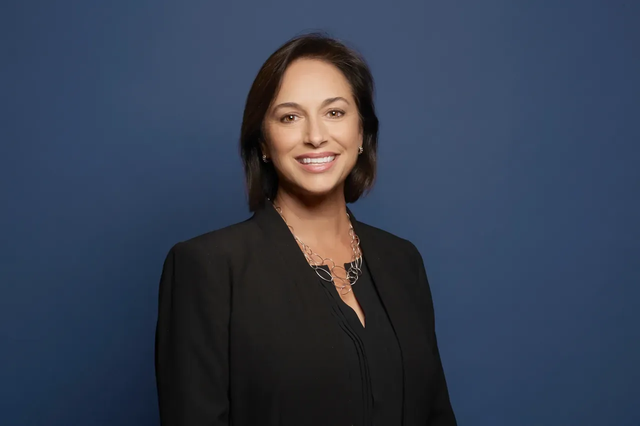 Professional headshot of Dr. Karen DeSalvo, Chief Health Officer at Google. She is smiling and wearing a black blazer and silver chain necklace against a solid blue studio background.