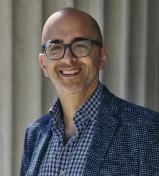 A professional portrait of David Edelman, CEO of Thrivable, smiling with glasses and a patterned blazer against a neutral architectural background in Ohio.