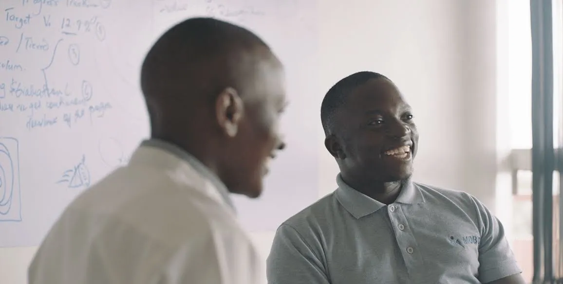Founder, Gerald Otim, smiles at a table with colleagues.