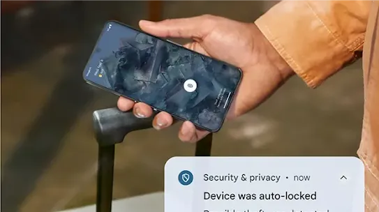 Auf einem Smartphone wird eine Sicherheitsbenachrichtigung mit dem Text „Gerät wurde automatisch gesperrt. Potenzieller Diebstahl erkannt.“ angezeigt. Das Smartphone wird von einer Person mit einer Hand gehalten – daneben befindet sich der Griff eines Rollkoffers.