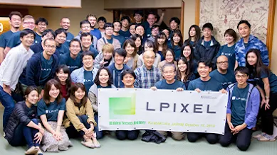 The team of LPixel surrounds a banner revealing their company’s name.