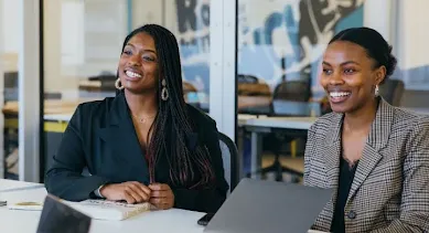 Two ladies sitting in a conference room.