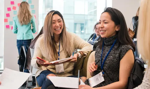 The two seated women in the group are conversing happily.