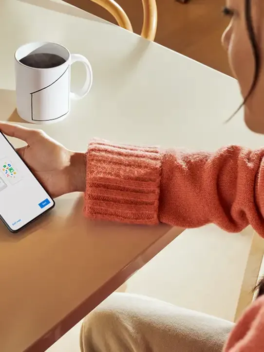 Frau sitzt mit Kaffee und hält Android Smartphone