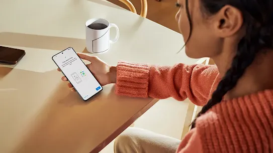 Frau sitzt mit Kaffee und hält Android Smartphone