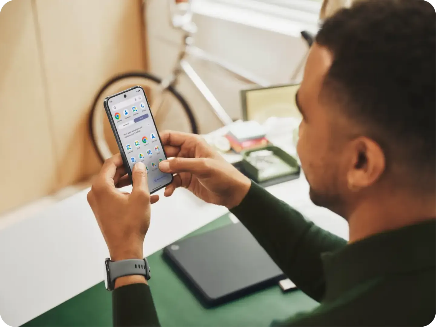 A man in a green shirt is holding his Pixel 9 in front of his face while seated at his desk.