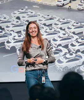 Una mujer sonríe mientras está de pie en un escenario y hace una presentación ante un grupo de personas
