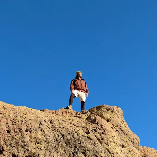 We see a person enjoying a view of the clear blue sky while on a hike.