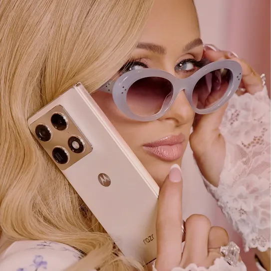 Paris Hilton gives a model-like look over her light blue sunglasses while holding a pink Motorola Razr phone to her ear.