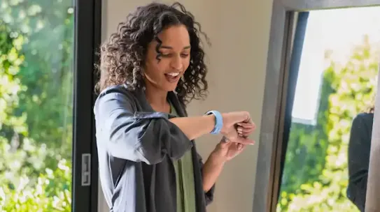 A woman is smiling while looking at her smartwatch.