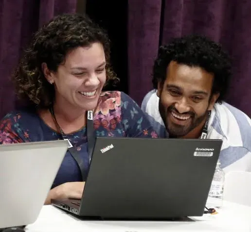 Uma mulher e um homem estão olhando para um laptop.