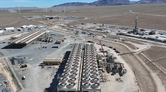 A  high-angle aerial view shows an expansive geothermal energy facility situated in a desert landscape with mountains in the distance