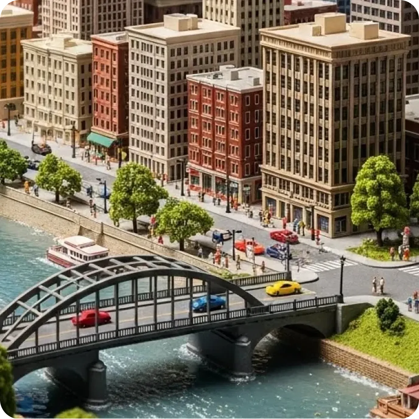 A highly detailed miniature model of a city featuring several multi-story buildings, a grey arched bridge over a blue river with tiny cars, a boat, and small green trees lining the waterfront.
