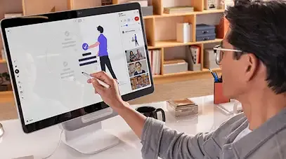 A person in glasses using a stylus on a large touchscreen monitor to collaborate a digital whiteboard during a video conference.