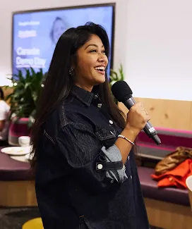 A young woman with a smile on her face speaks into a microphone while wearing a black shirt.