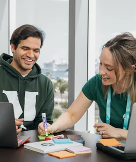A seated man and woman, with the woman writing on sticky notes.