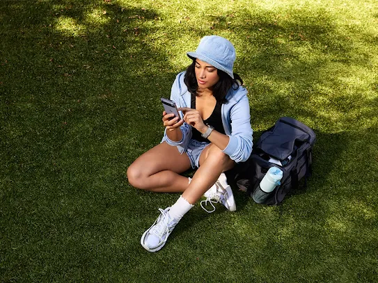 Woman using her phone while outside, in a field or park.
