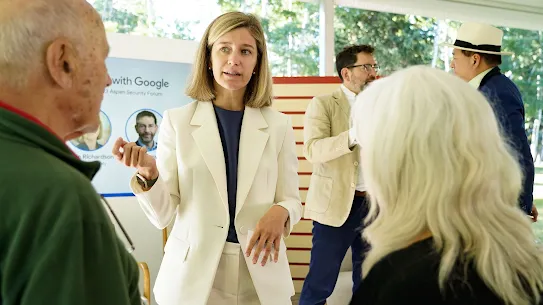Laurie Richardson, Google’s VP of Trust and Safety, engaging in conversation with attendees at the 2023 Aspen Security Forum. She is wearing a white suit and gesturing while speaking. In the background, "Safer with Google" signage and other forum participants are visible under a bright outdoor tent.