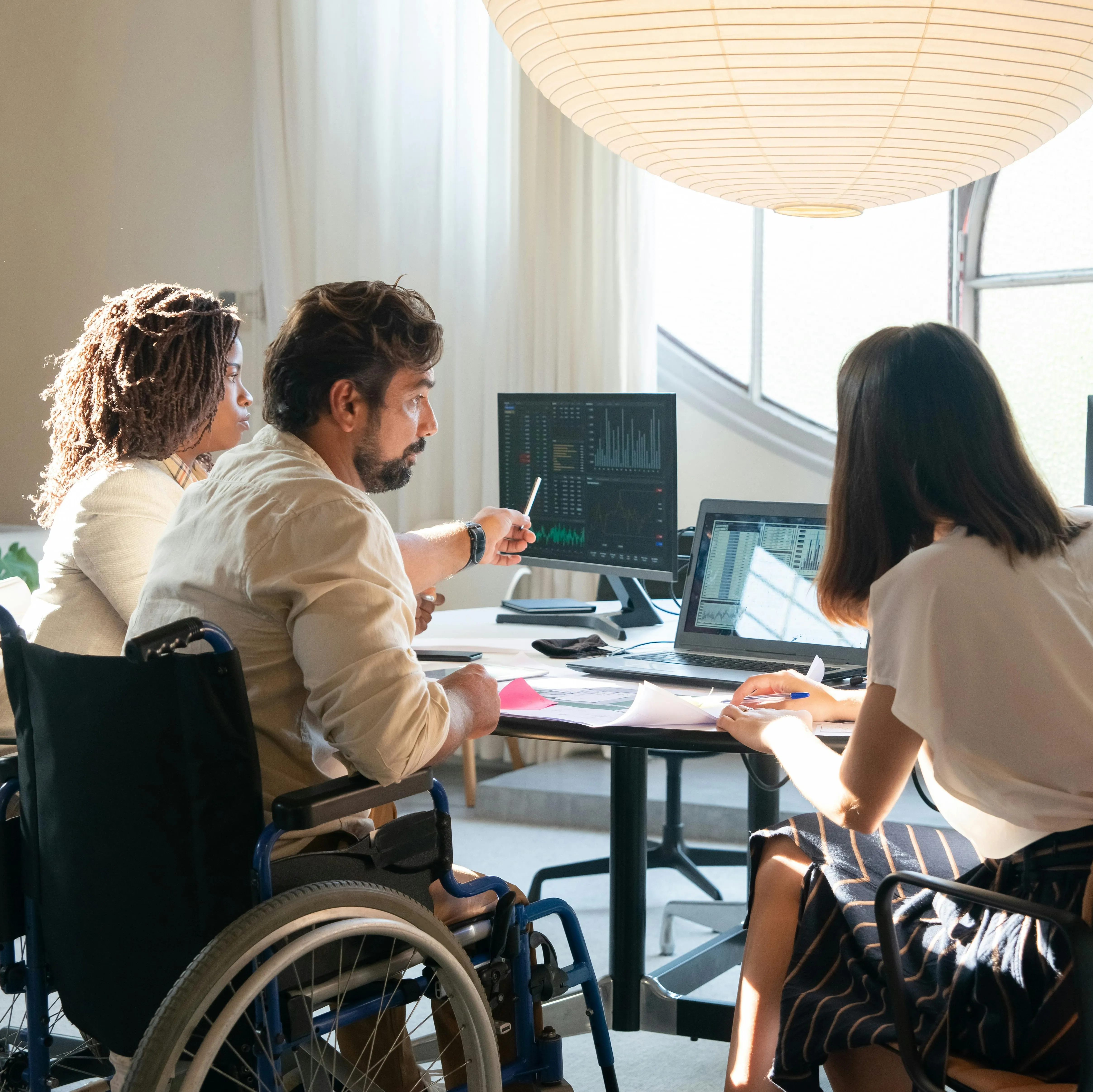 A group of three people sit around a desk with computers on it.