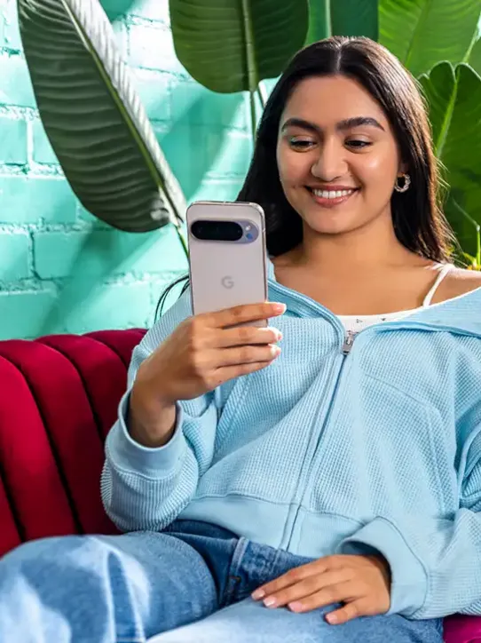 Mulher sentada em um sofá sorrindo e usando um smartphone.