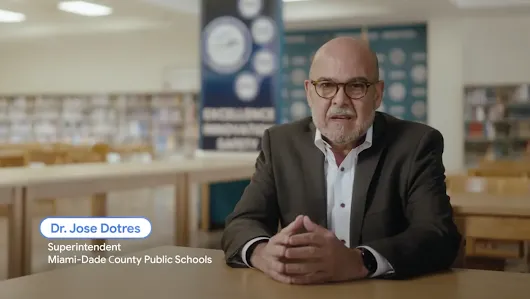 Dr. Jose Dotres, Superintendent of Miami-Dade County Public Schools, speaking directly to the camera while seated at a wooden table in a school library. A digital lower-third graphic identifies him by name and title. Behind him, a blurred banner reads "Excellence, Innovation, Safety."