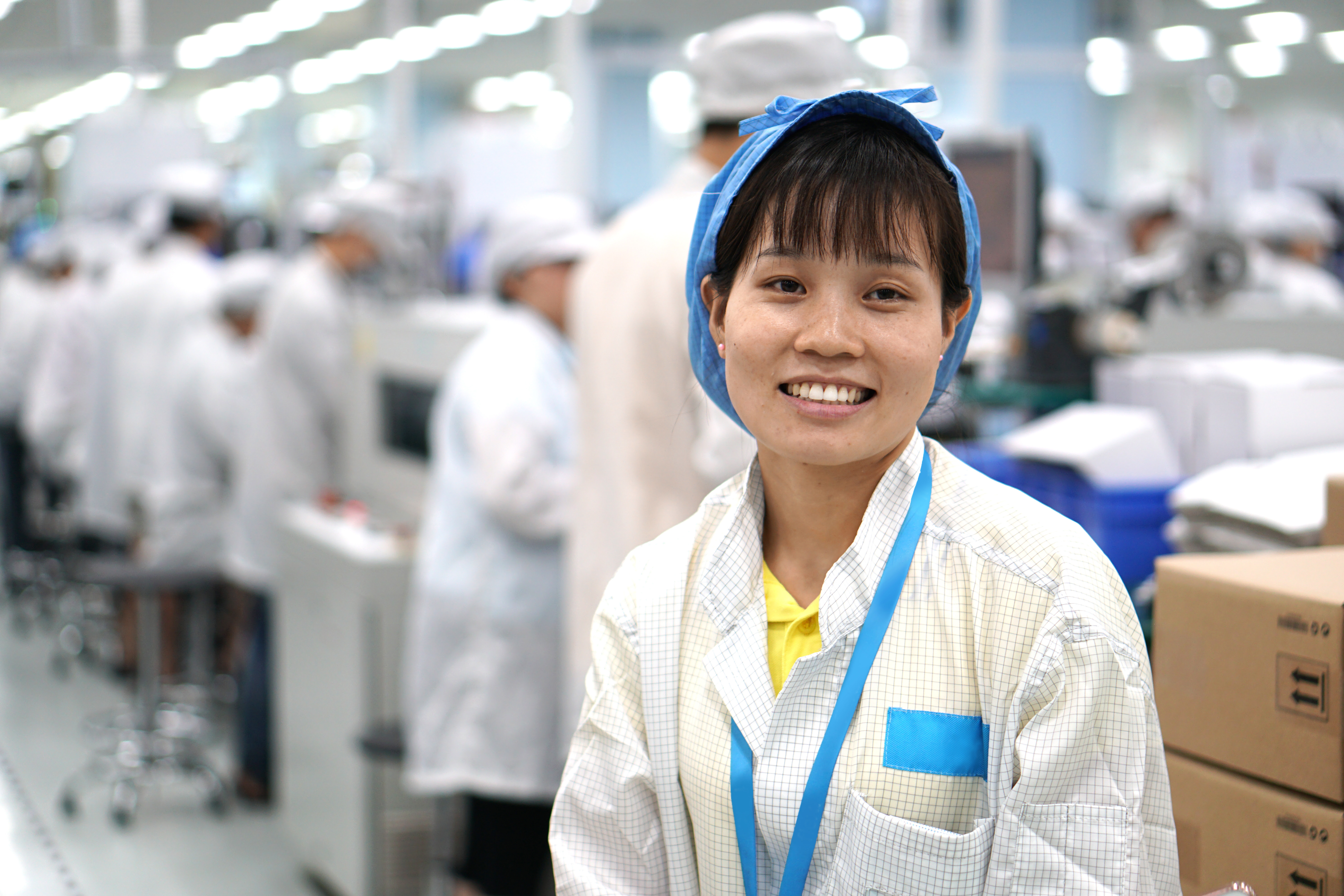 A person smiling at the camera and wearing a factory uniform.
