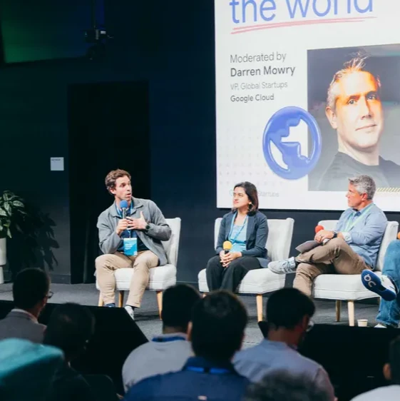 A moderator hosts a panel of five Google for Startups founders who are seated on a stage in front of a large screen