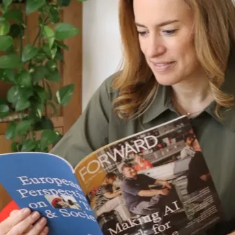 Debbie Weinstein, Vice President, reading a magazine titled "FORWARD: European Perspectives on Society" that features a section on making AI work for everyone.