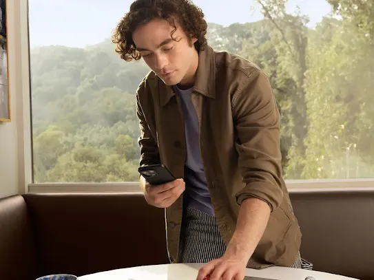 Man using an Android phone. He is standing over a desk with several documents and notepads and is pointing the device