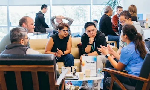 A group of people are engaged in a collaborative discussion at a startup forum in a modern co-working space.
