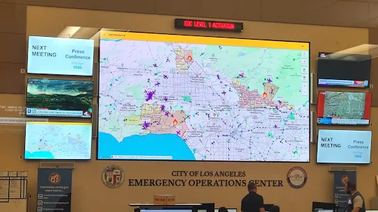 Large digital map display inside the City of Los Angeles Emergency Operations Center showing active wildfire monitoring, flight paths, and evacuation zones on Watch Duty.