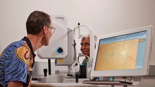 Doctor looking at retina scans with patient in front of machine