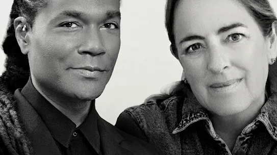 A black and white portrait shows two people positioned closely together against a plain, light-colored background