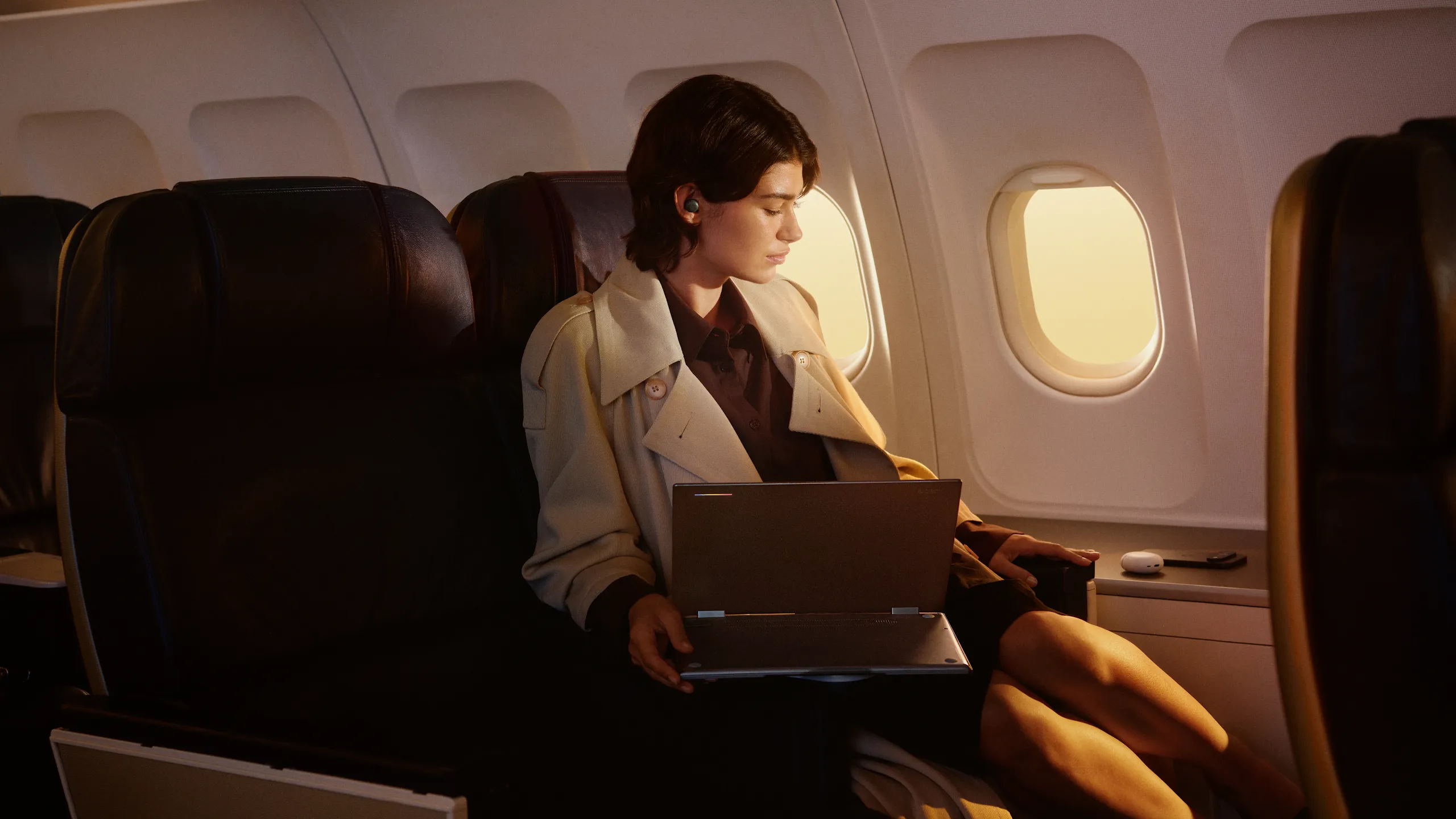 A person seated in an airplane cabin, opening a laptop.