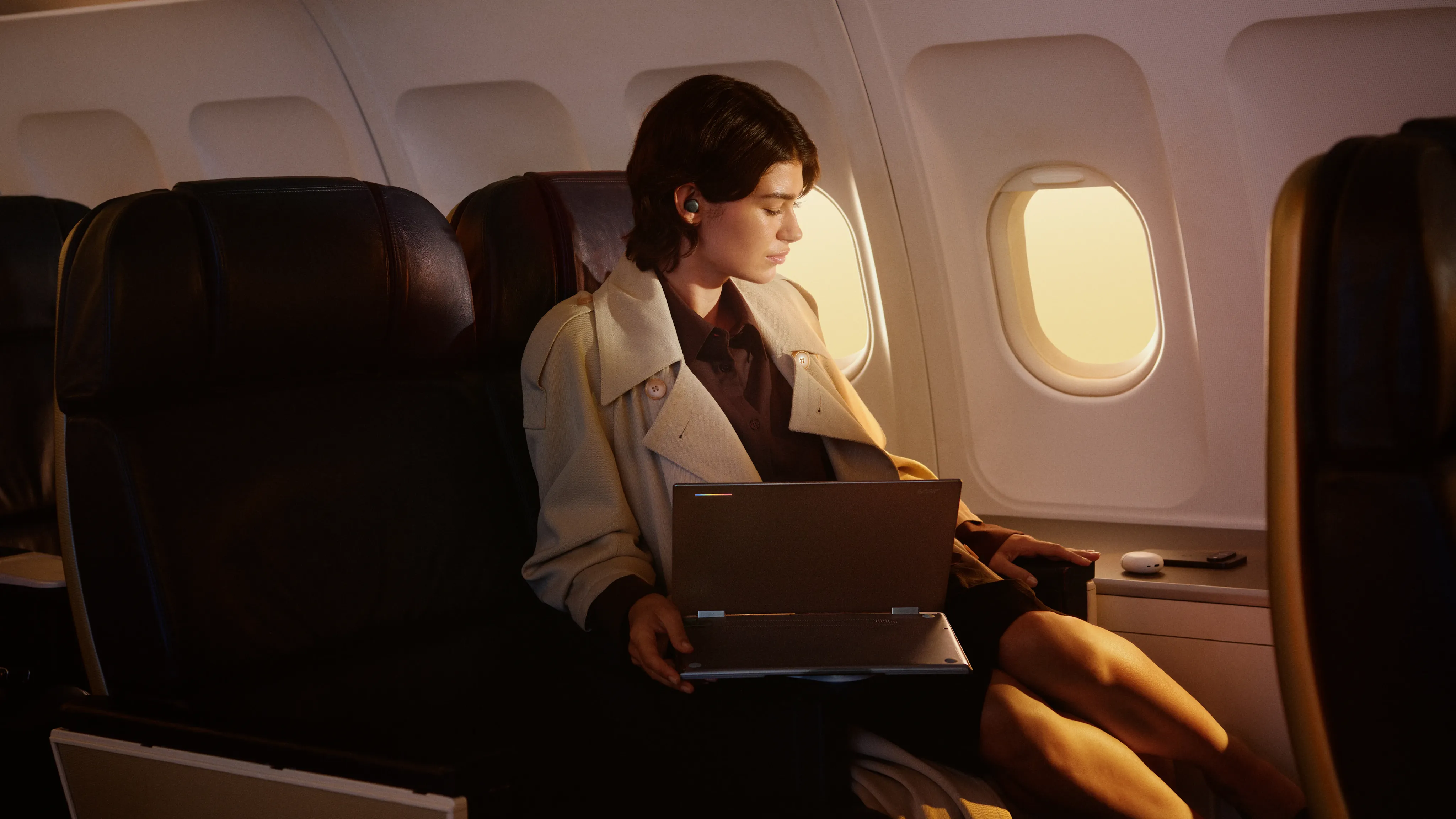 A person seated in an airplane cabin, opening a laptop.