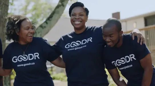 Group of coworkers wearing matching shirts smiling and holding shoulders