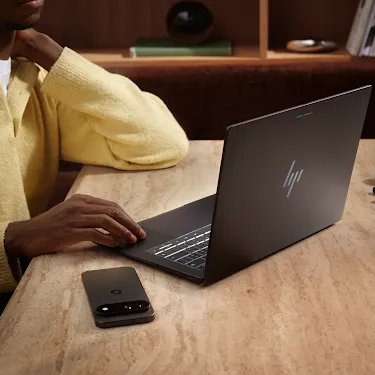 Person using a Googlebook at a desk with a phone nearby.