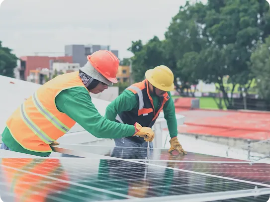 Two technicians in high-visibility vests and hard hats installing or maintaining solar panels on a building rooftop.