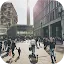 A busy public square in Berlin with pedestrians walking under a bright sun, featuring the Berlin TV Tower in the distance.
