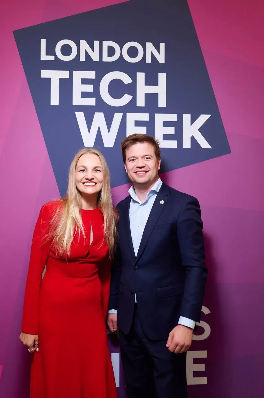 Antonina Iermeichuk, Co-founder and COO of DEUS Robotics, and Pavlo Pikulin, Founder and CEO, smiling together in front of a purple London Tech Week backdrop. Antonina is wearing a vibrant red dress, and Pavlo is in a navy blue suit.