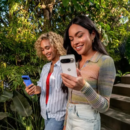 Two women using their Android devices outdoors, with trees in the background.