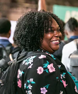 Una mujer sonriente con un top negro de flores y una mochila.