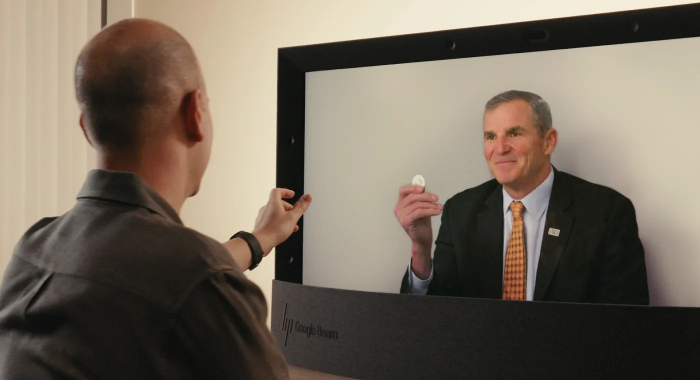 A carousel of images and videos shows the evolution of Google Beam devices over time.
A person holds up a coin to illustrate the life-like 3D capabilities of Google Beam.
